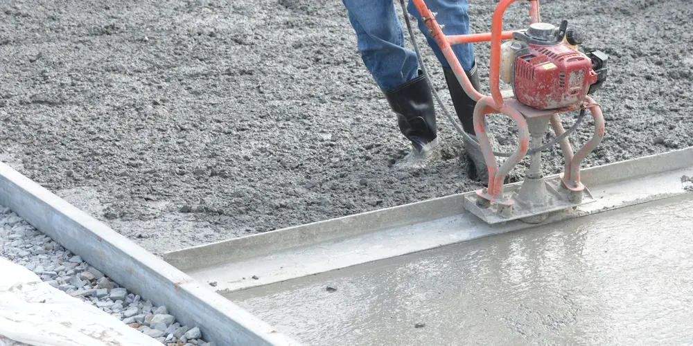 A power screed leveling fresh concrete between forms.